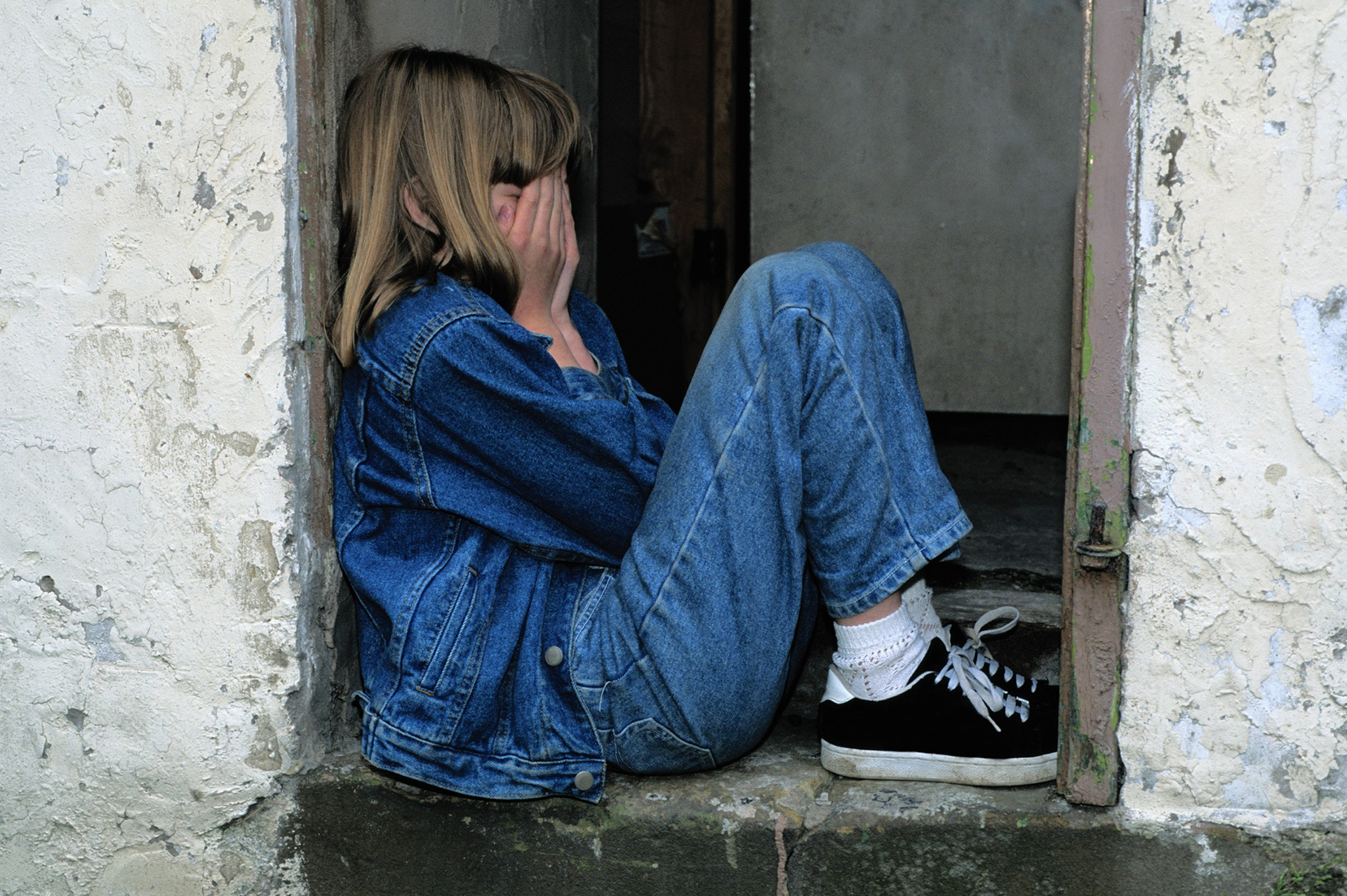 Mädchen sitzt weinend im Türrahmen